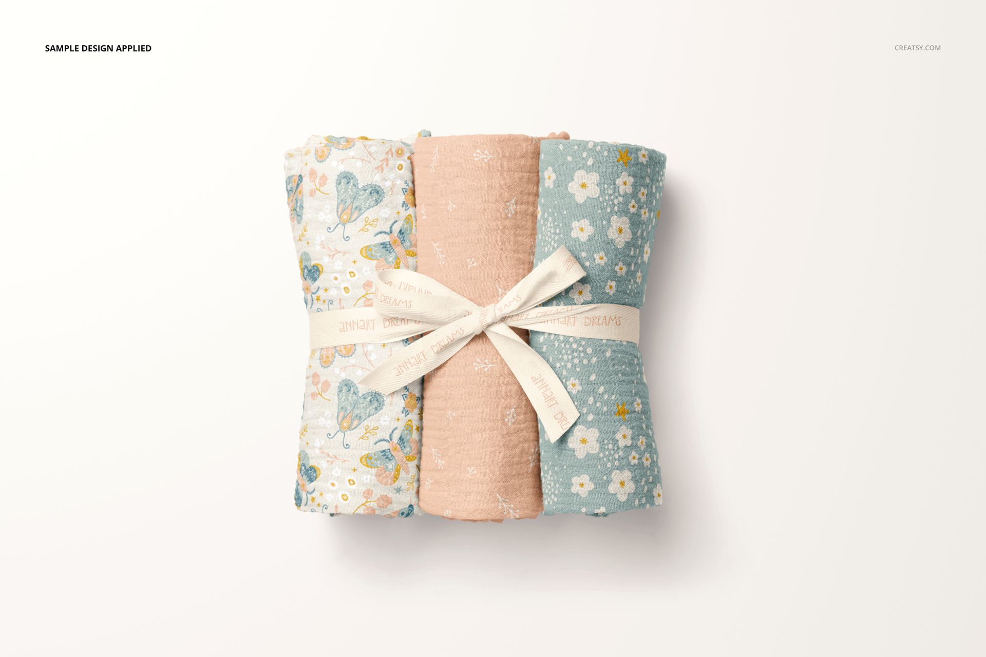 Three crinkle muslin swaddle blankets rolled side by side, featuring floral and dotted patterns in pastel colors.