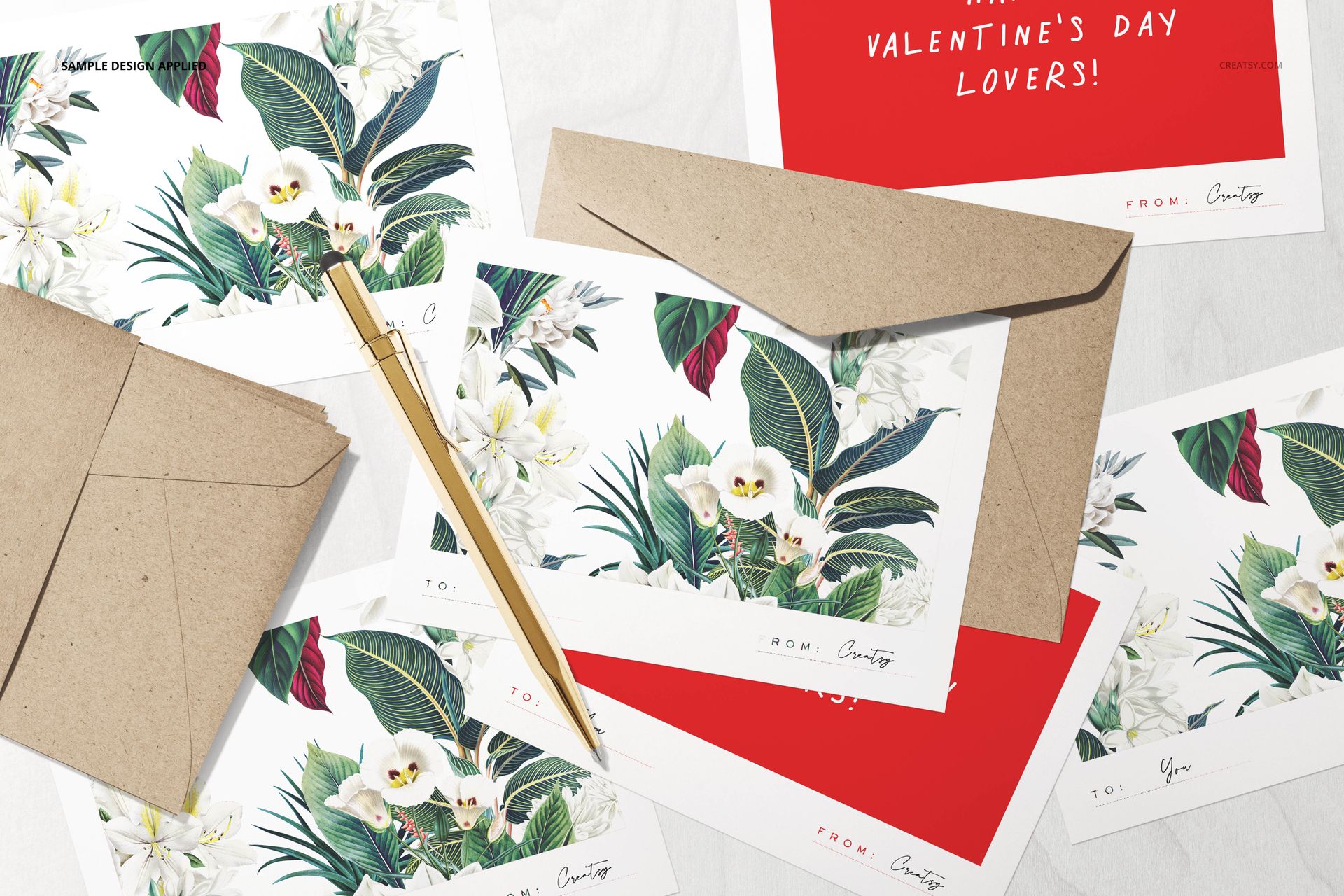 Top view of stationery mockup set with floral cards, kraft envelopes, gold pen, and red Valentine’s card on white surface.