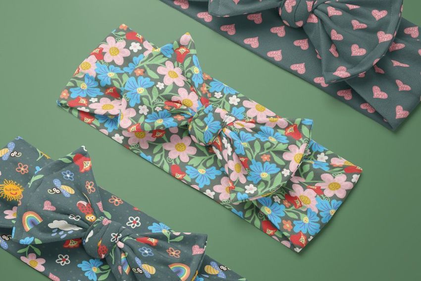 Kids adjustable bow tie style headband mockup featuring floral and whimsical patterns on green background, viewed from above.