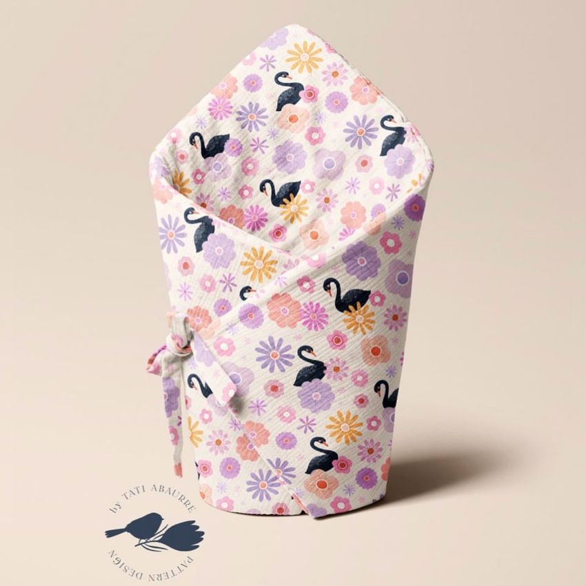 Newborn swaddle wrap mockup featuring a pastel floral and swan pattern, displayed upright on a neutral beige background.