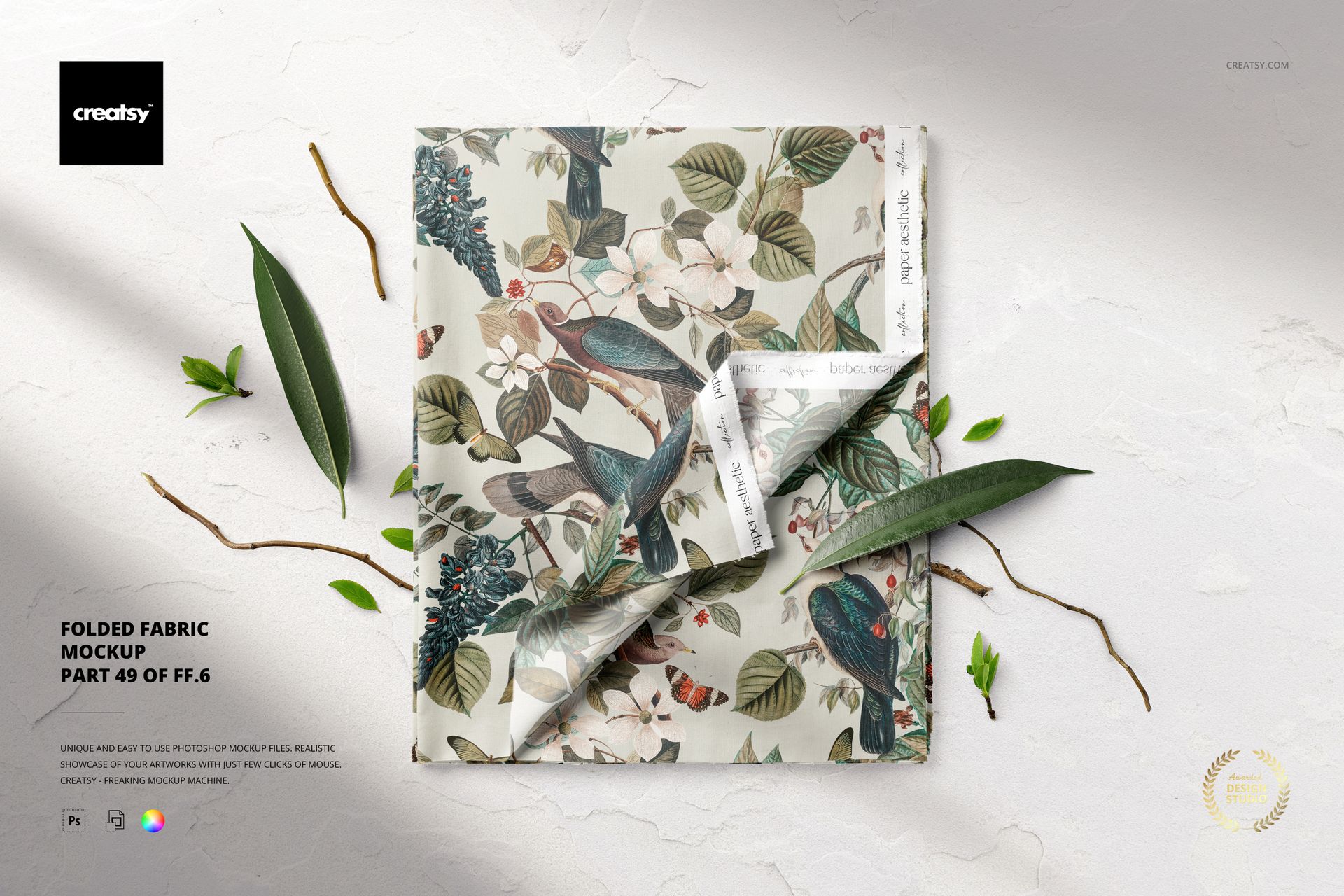 PSD mockup of folded fabric featuring a colorful floral and bird design, shown from a top-down perspective with leaf props.