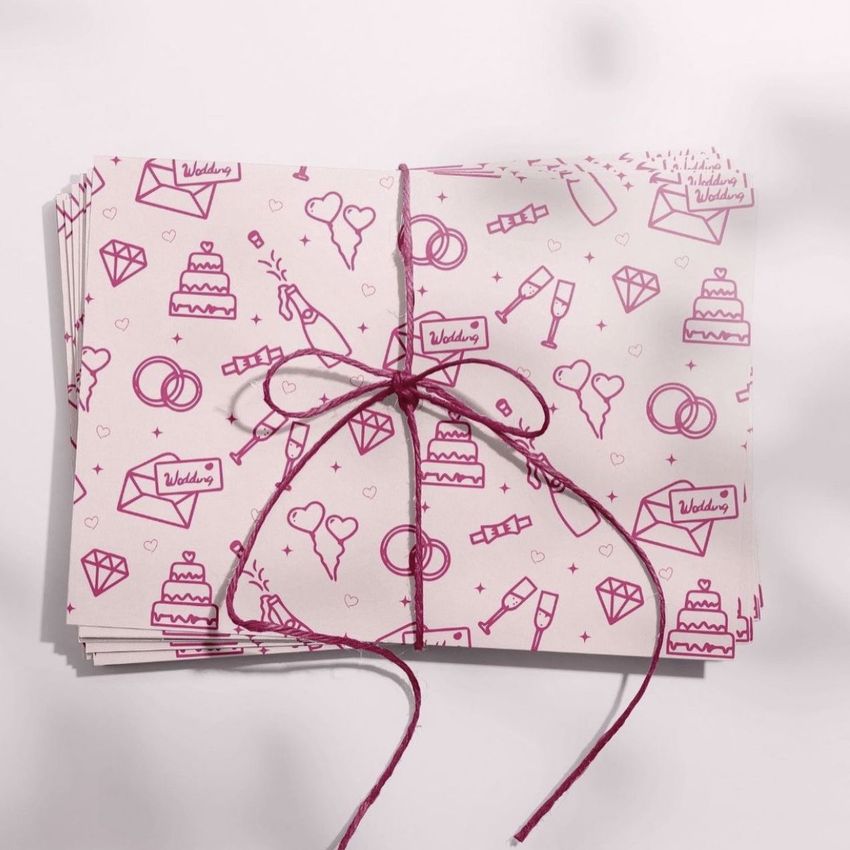 Stack of stationery cards with wedding-themed pink line illustrations, tied together with a pink string on a light surface.