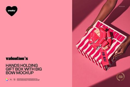 Top view of hands presenting a striped gift box with a shiny red bow on a solid pink background, PSD mockup.