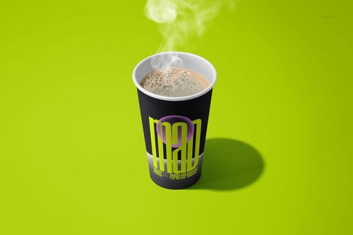 Single paper cup mockup featuring steam rising from coffee, black sleeve with vivid yellow design, set on green surface.