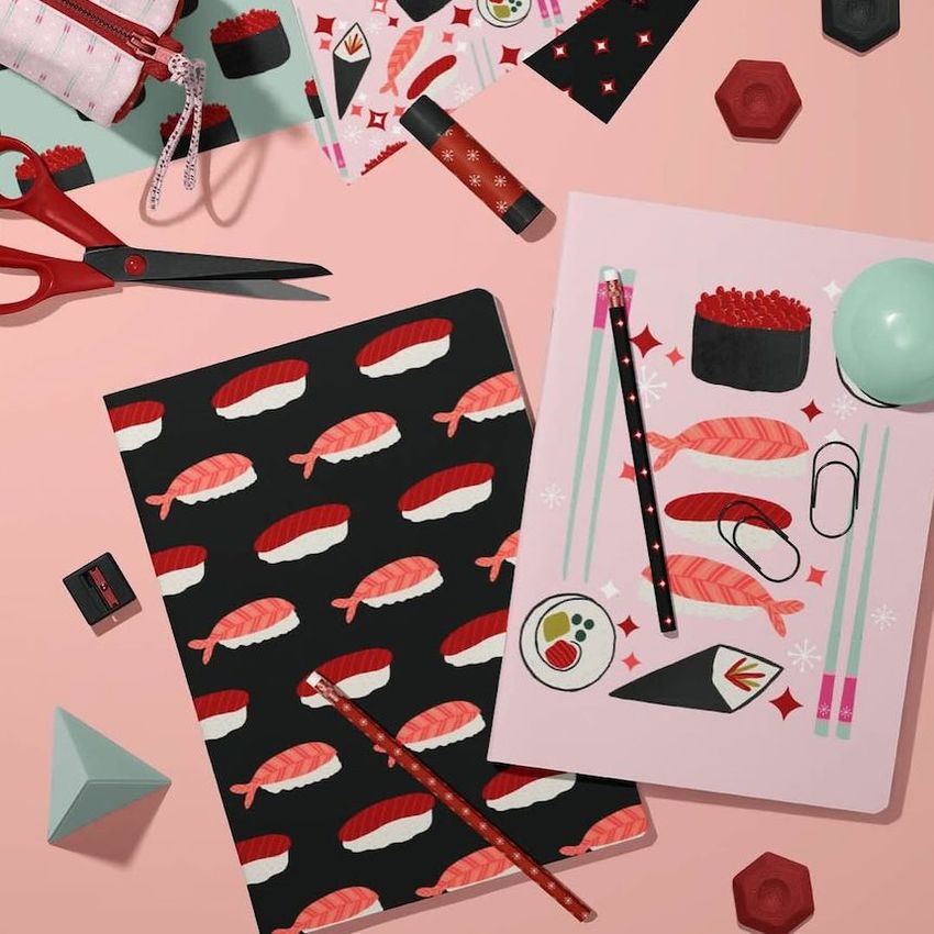 Stationery mockup featuring two A4 notebooks with sushi-themed covers, pencils, scissors, and geometric props on a pink surface.