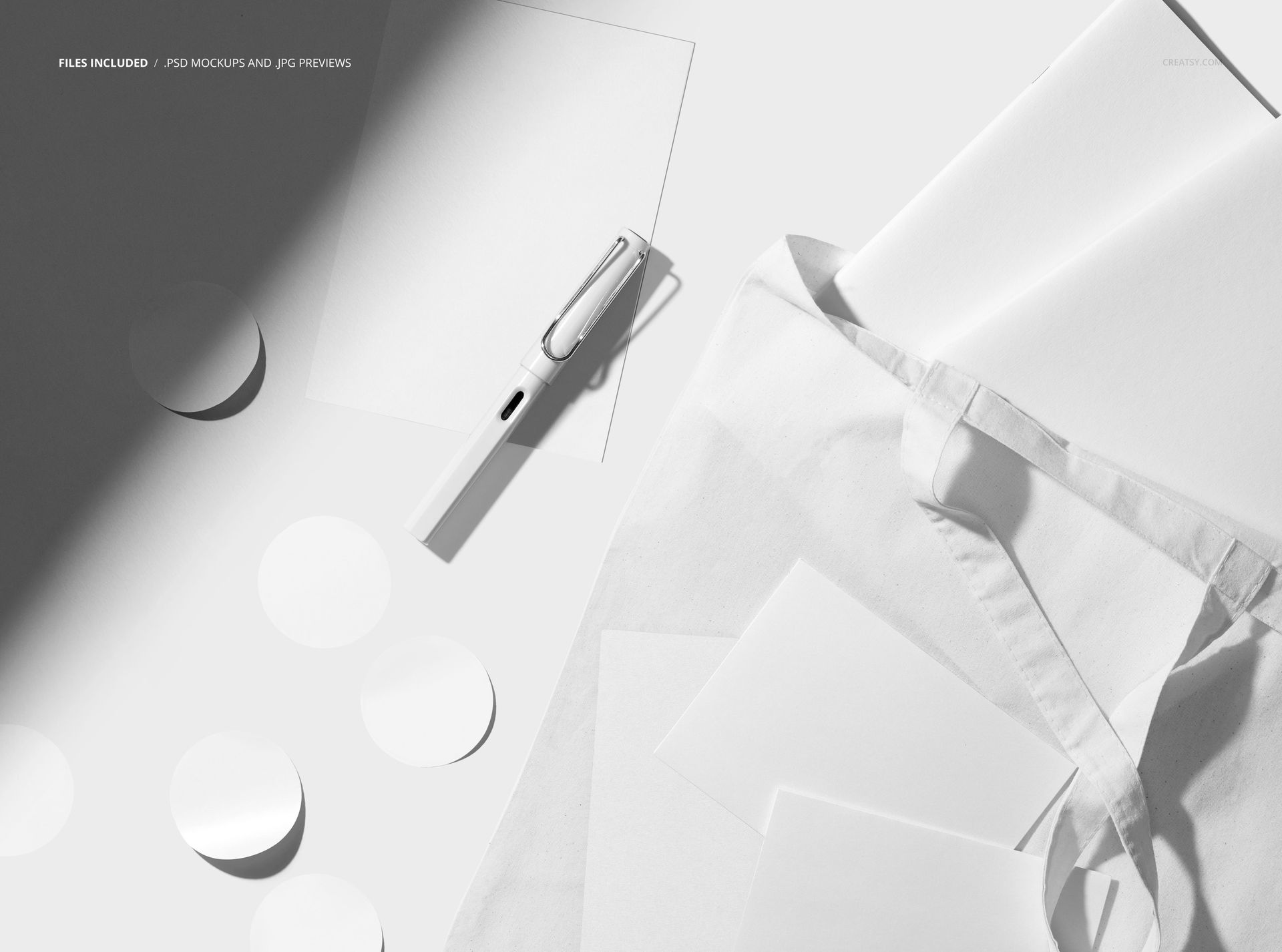 White tote bag mockup with assorted stationery objects, such as paper circles, sheets, and a pen in bright lighting.