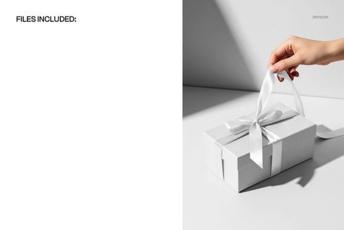 Luxury gift box mockup featuring a white box with a satin bow, viewed from above with a hand adjusting the ribbon.