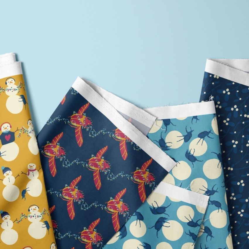 Folded fabrics mockup featuring three fabric pieces with snowman and beetle patterns in blue, yellow, and navy tones.