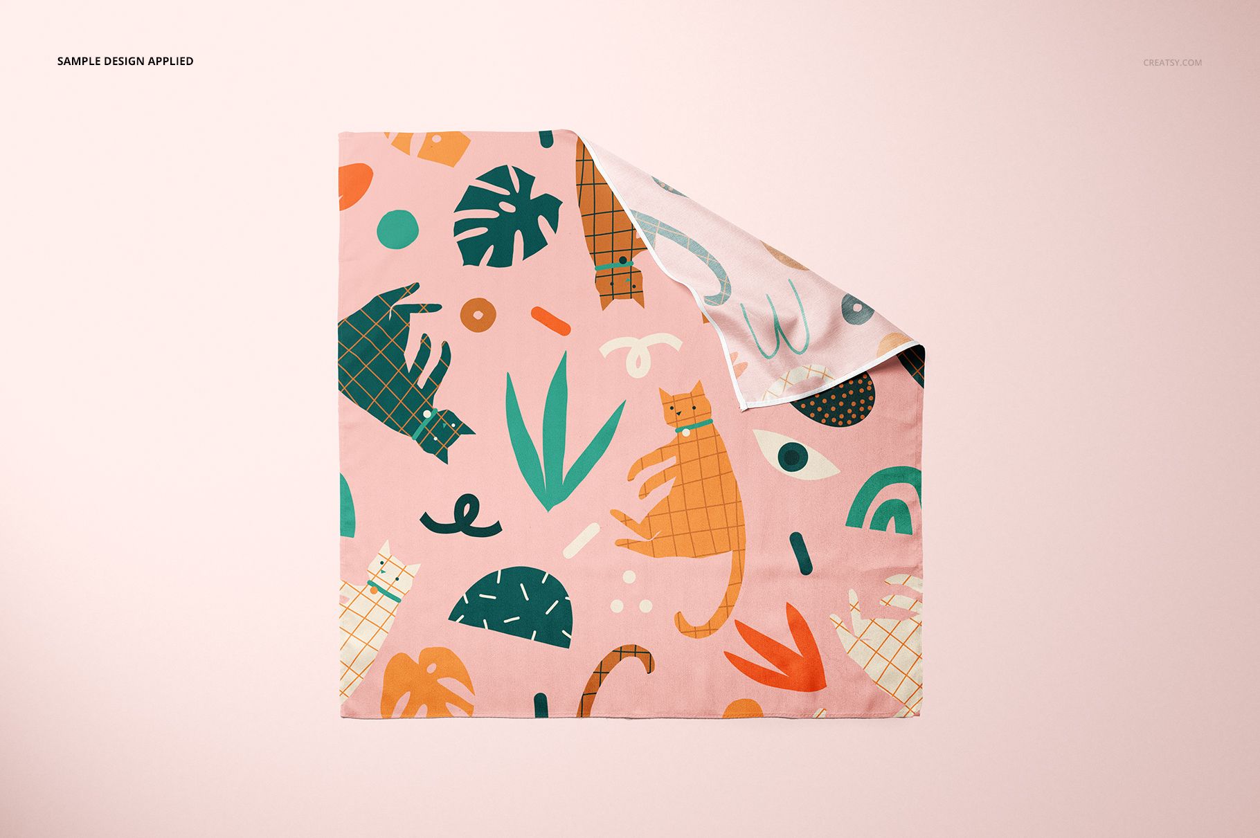 Flat lay of a pet bandana mockup featuring playful cat illustrations and green leaves on a soft pink surface.