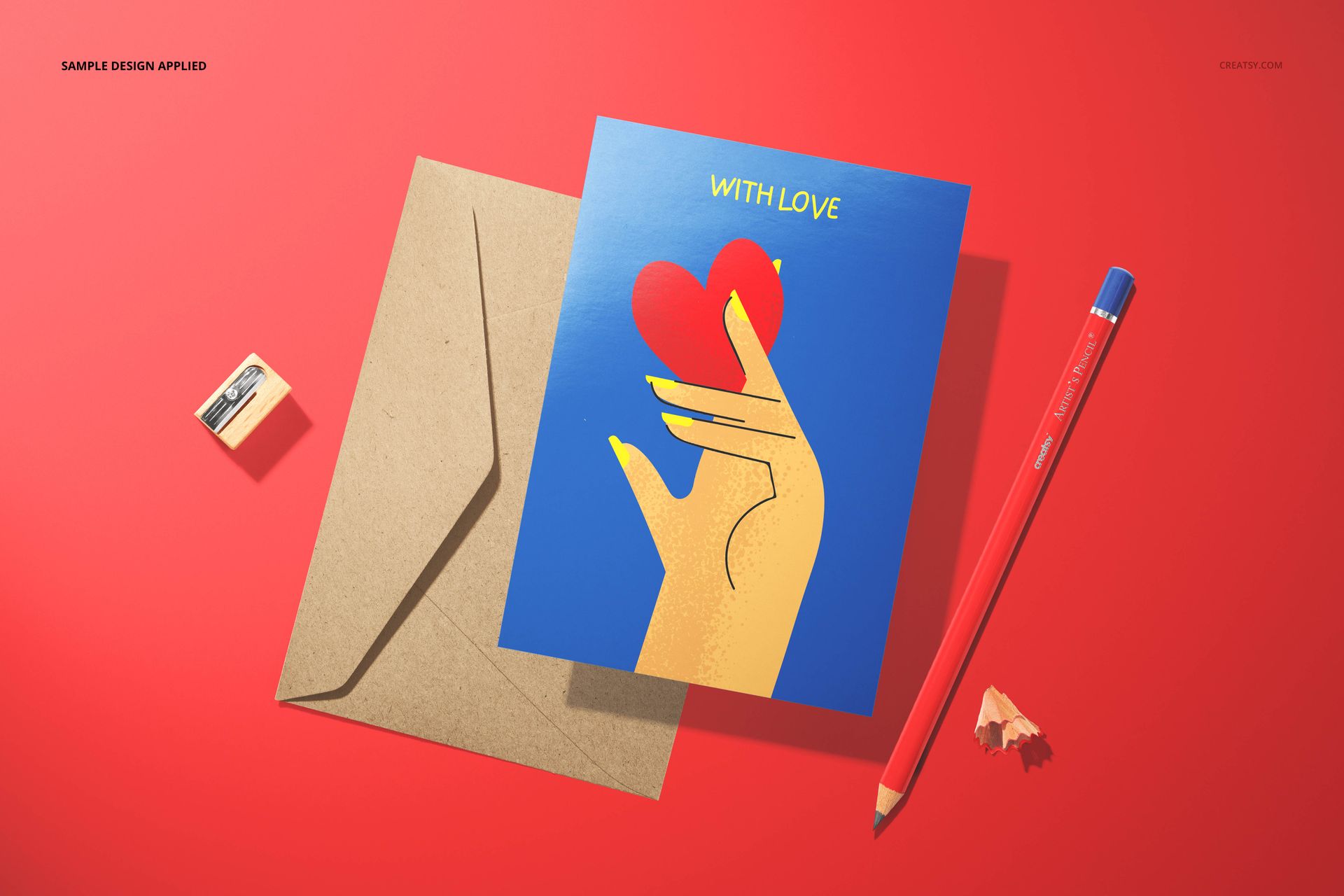 Valentine's card mockup featuring a blue card with a hand and heart illustration, kraft envelope, and red pencil on a red surface.