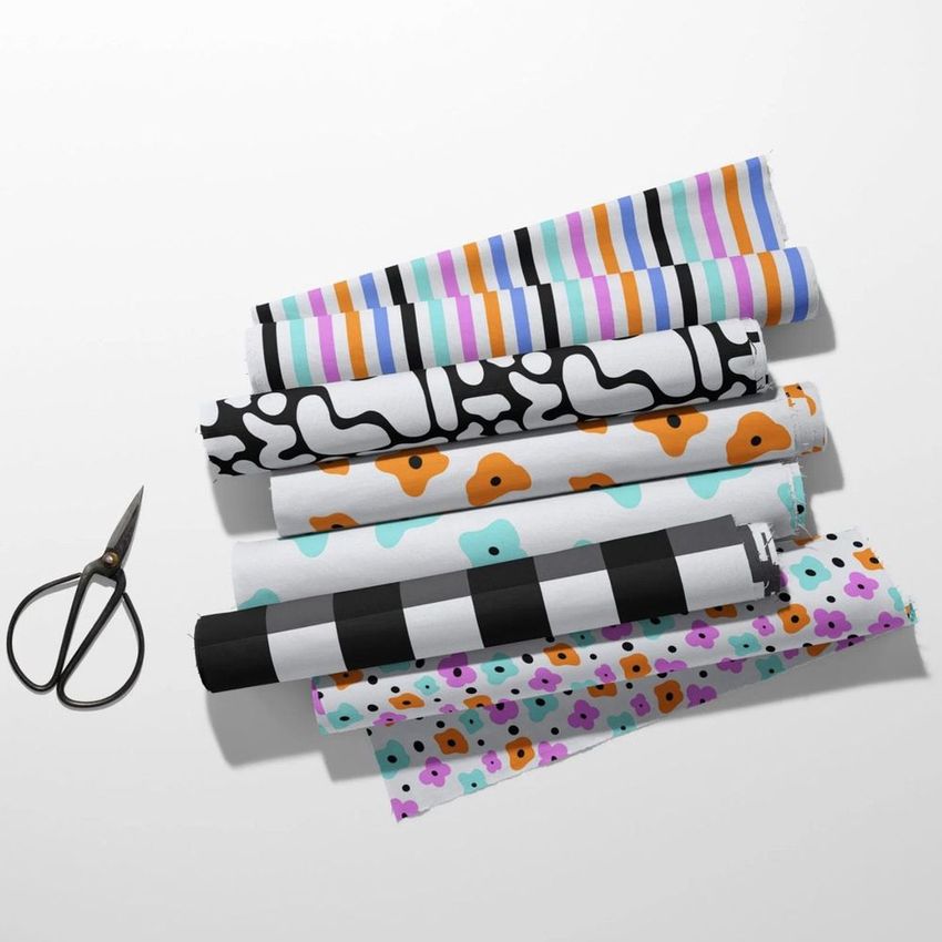 Fabric rolls mockup showing six patterned fabrics arranged in a row on a white surface, with scissors beside them.