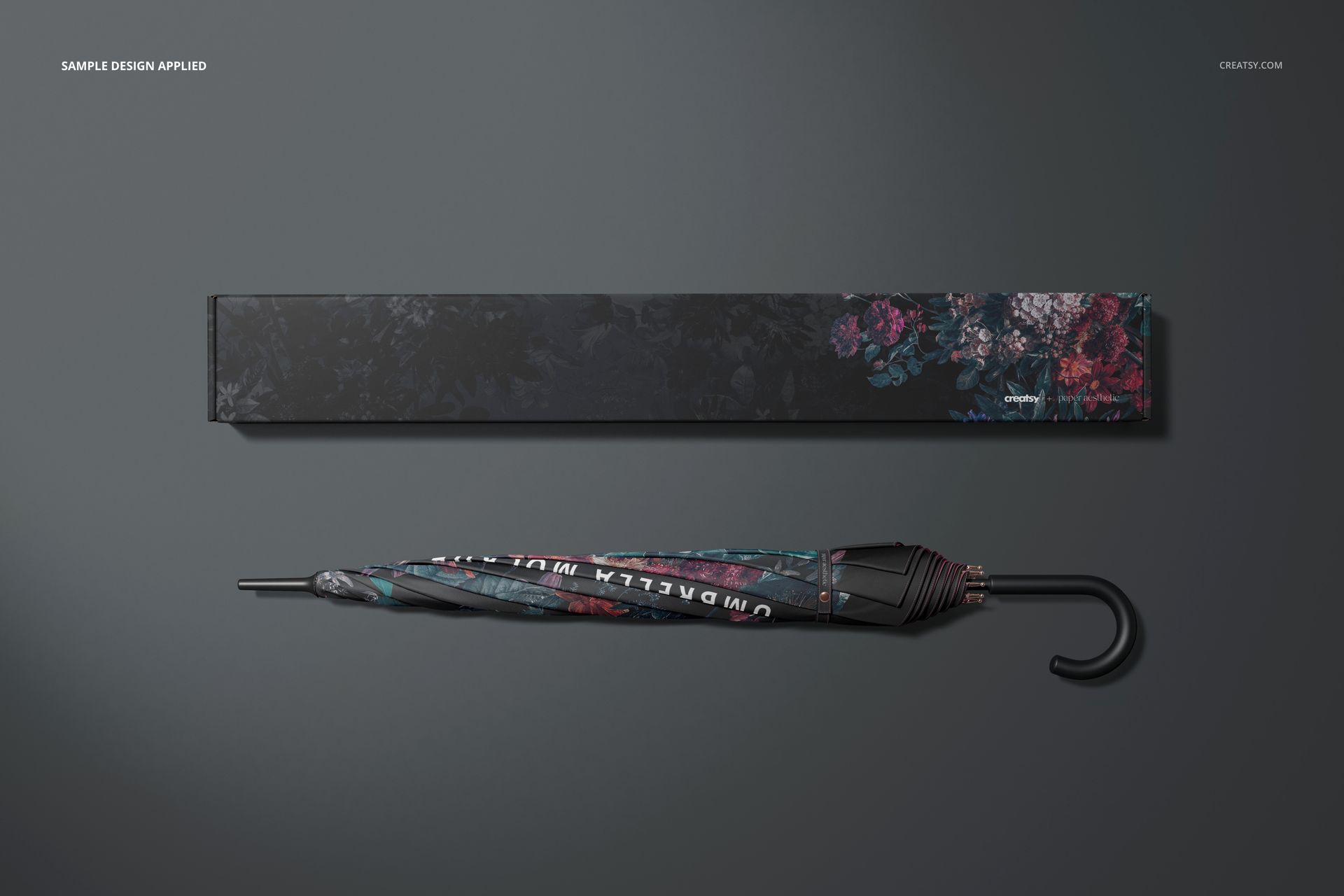 Umbrella and packaging box mockup featuring dark floral designs, shown in a top view arrangement on a gray tabletop.
