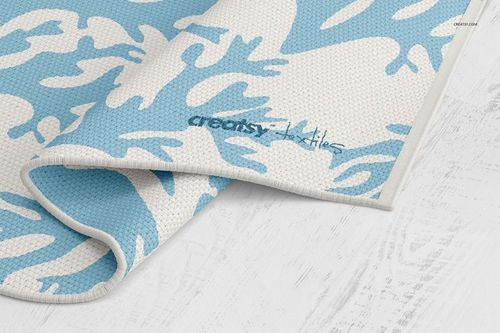 Close-up of a woven rug mockup featuring a blue and white abstract design, displayed on a pale wood surface.