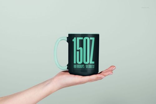 Front view of a 15oz ceramic mug mockup with a matte dark green finish, held by a hand against a light background.