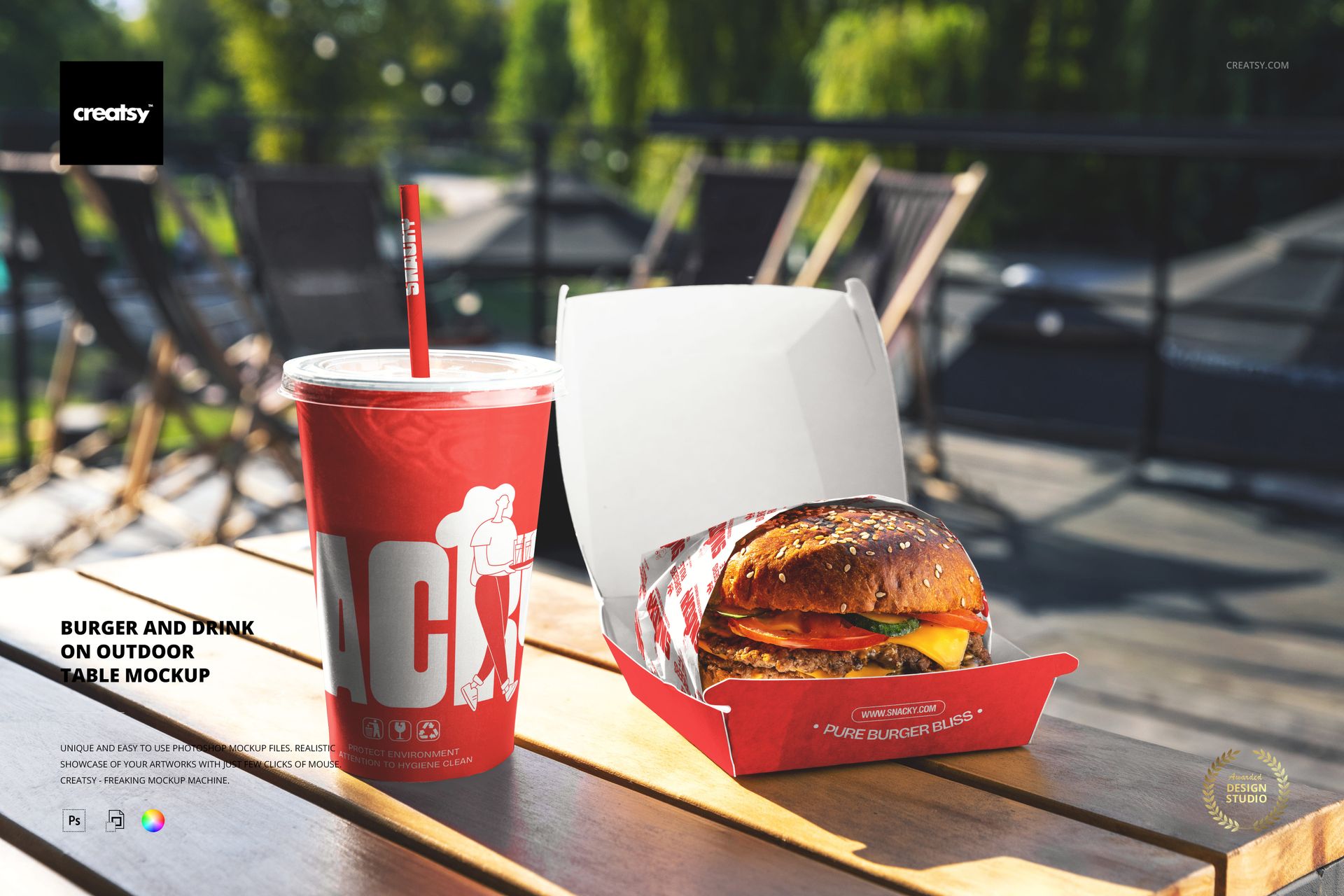 PSD mockup showing a burger in an open box and a red beverage cup placed on a wooden table outdoors with patio chairs.