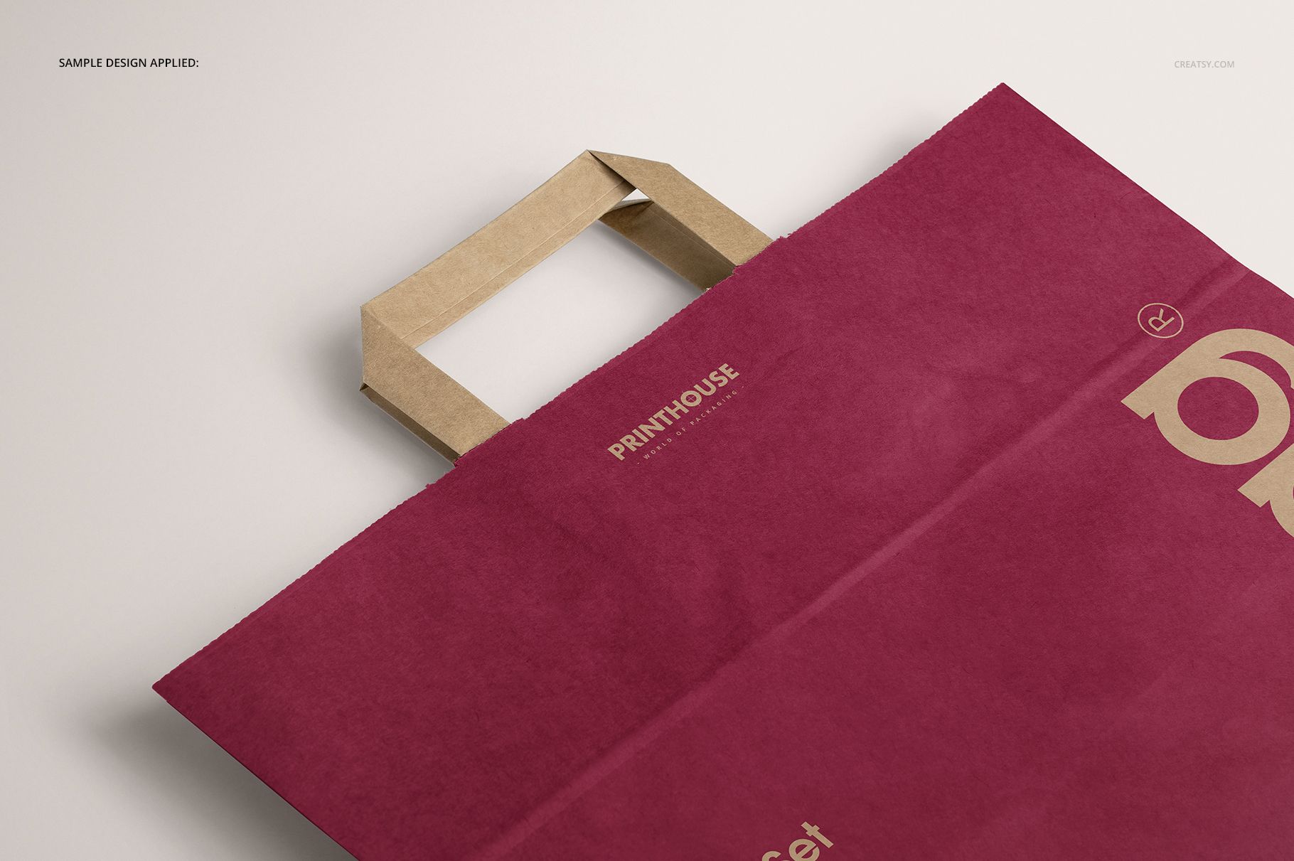 Folded handle kraft paper bag mockup with a deep red color, shown from a top angle on a light surface.