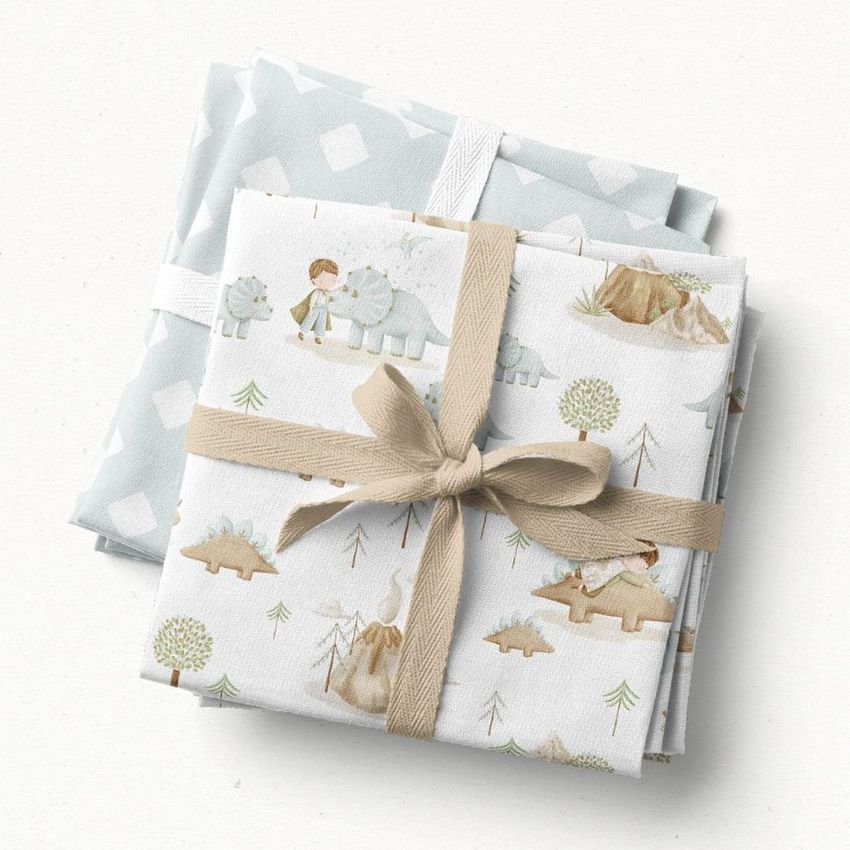 Fabric stack mockup featuring two folded fabric pieces, one with dinosaur and child illustrations, tied with a beige ribbon on a light surface.