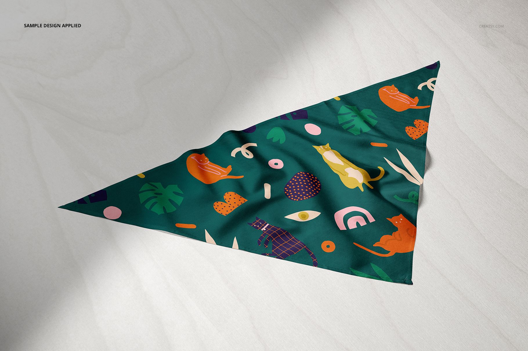 Pet bandana mockup featuring a green fabric with playful cat illustrations and tropical leaves, shown from above.