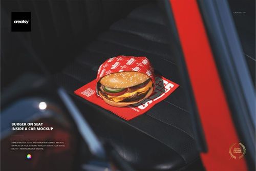 PSD mockup showing a hamburger wrapped in red patterned paper, resting on a dark car seat with window trim visible.