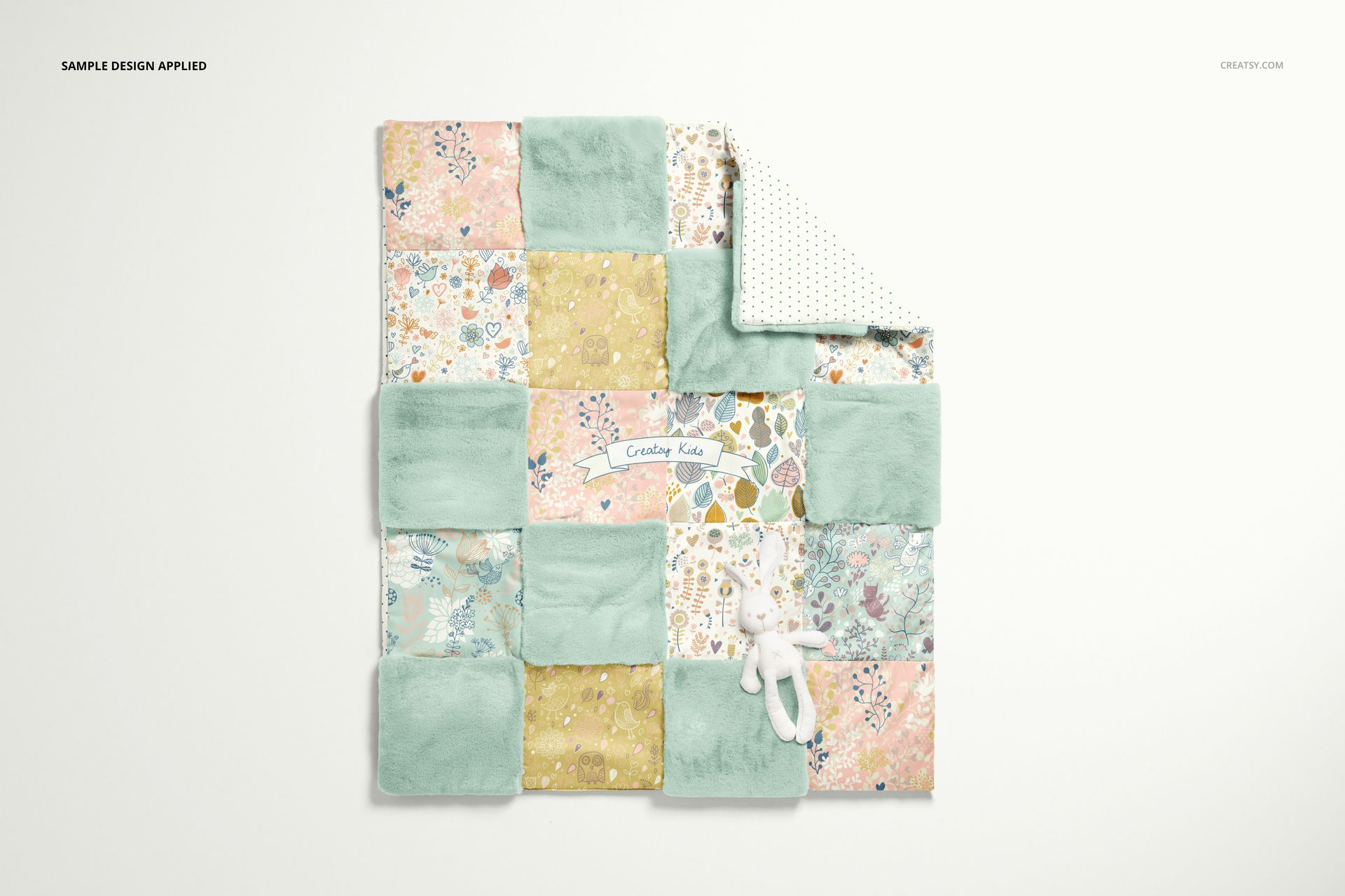 Baby patchwork quilt mockup with mixed pastel fleece and printed squares, displayed flat with a plush toy on white surface.