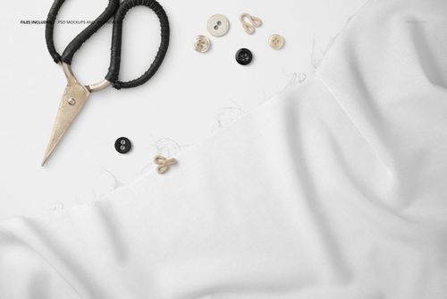 Wrinkled white textile mockup with scattered sewing tools like scissors, buttons, and hooks on a light background.