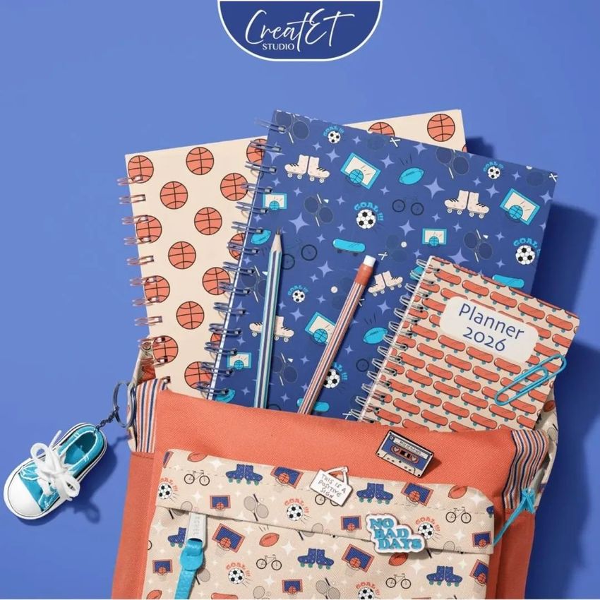 School backpack mockup with spiral notebooks featuring sports and vehicle patterns, pencils, and a small sneaker keychain on a blue background.