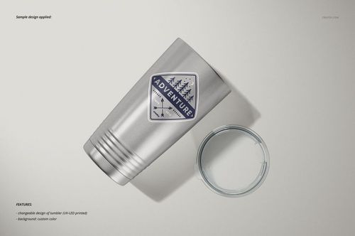 Stainless steel tumbler with a geometric mountain and tree design, shown from a top angle next to a clear plastic lid.