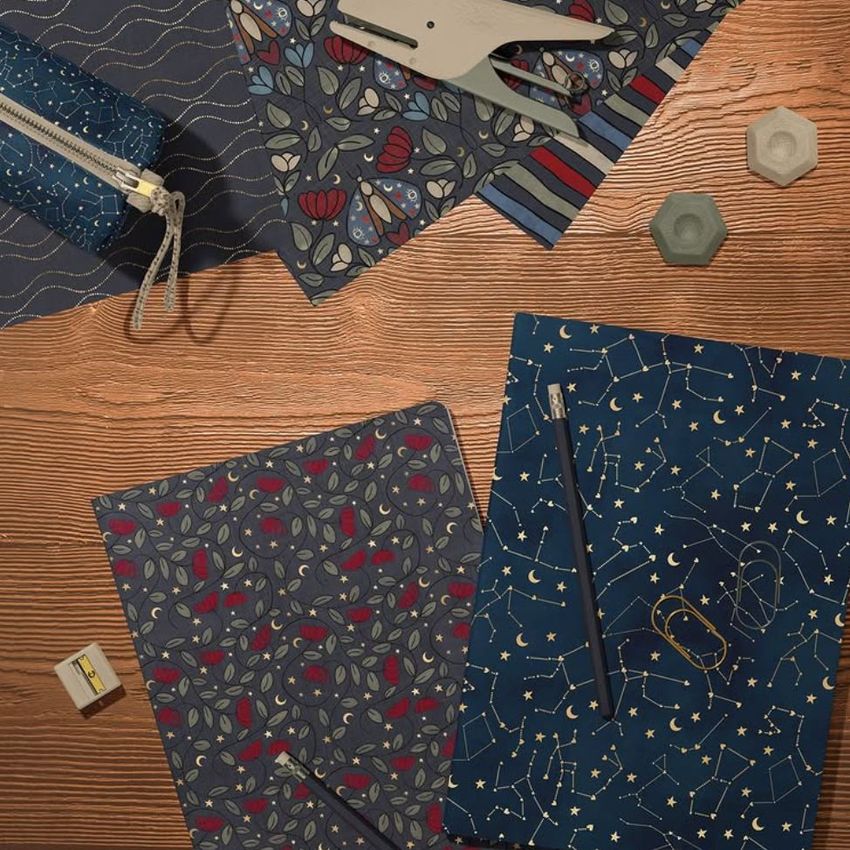 Stationery mockup featuring two classic A4 notebooks on a wooden surface, decorated with botanical and constellation patterns.