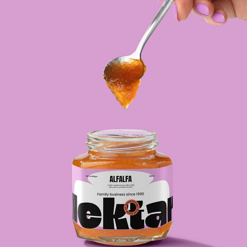 Apricot jam jar mockup on a purple background with a hand holding a spoonful of jam above the open jar, label with bold text.