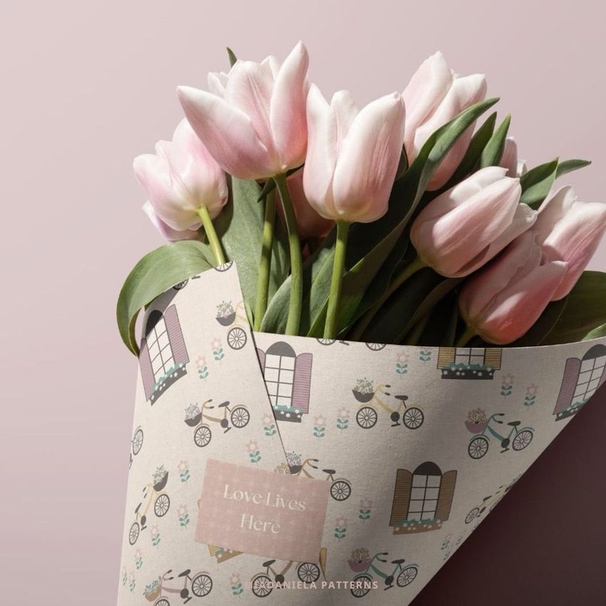 Packaging cone mockup featuring pink tulips wrapped in patterned paper with illustrated windows, bicycles, and flowers on a soft pink background.