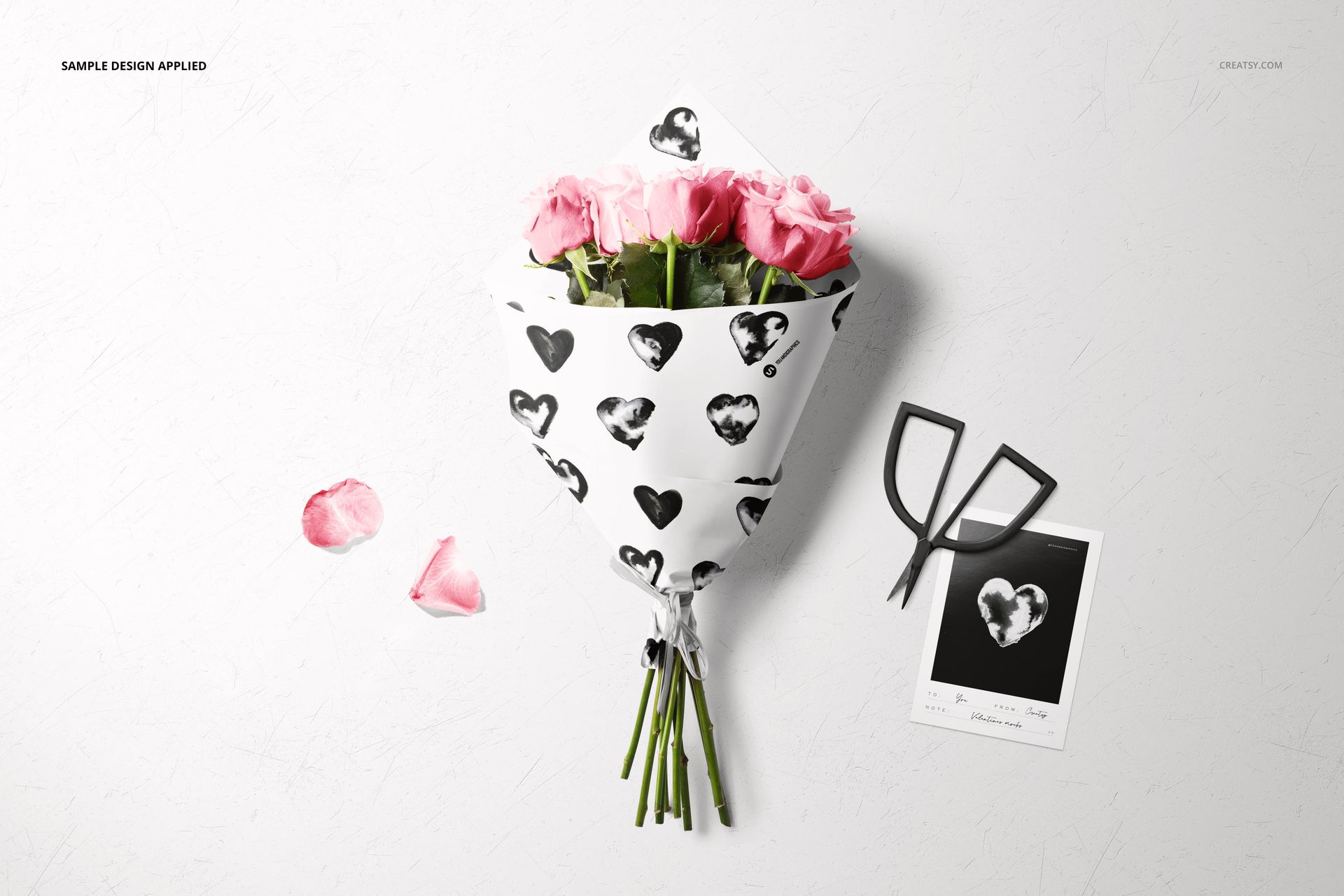 PSD mockup showing a bouquet of pink roses in decorative wrapping paper, with a monochrome card and raffia ribbon nearby.