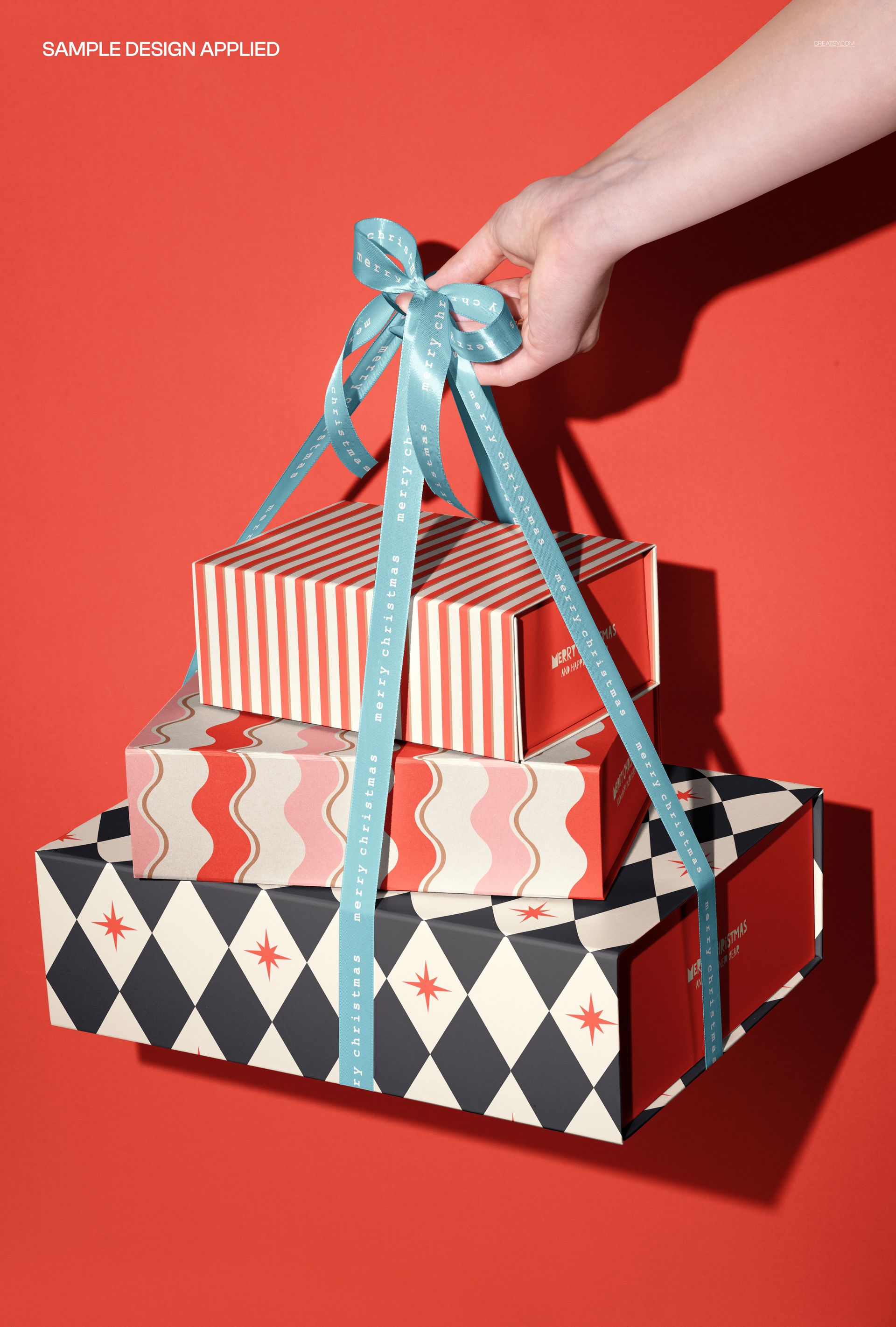 Front view of a hand lifting three decorative gift boxes with various patterns using a blue ribbon, PSD mockup scene.