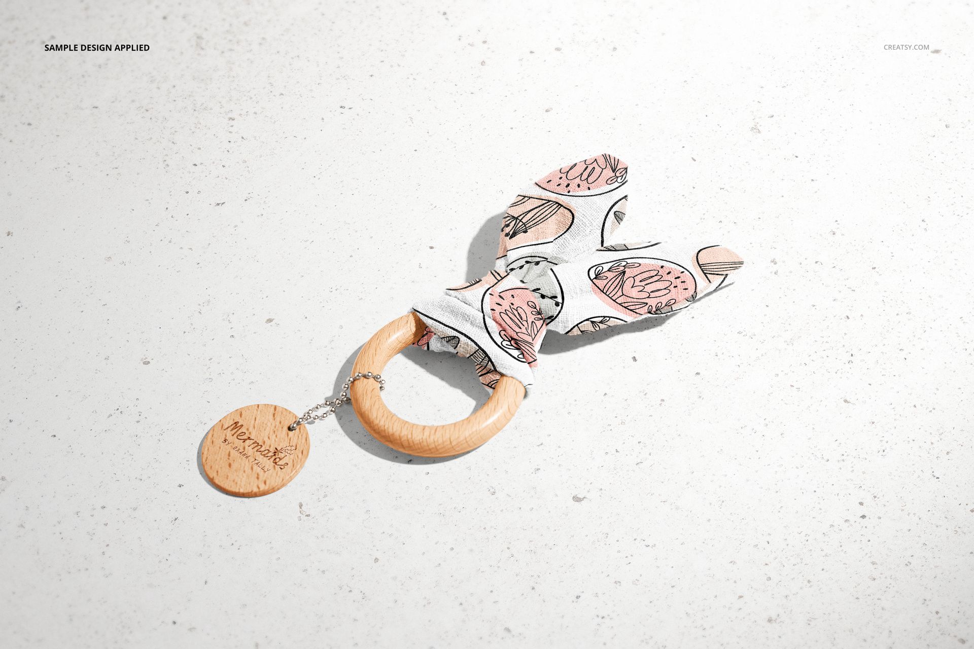 Wooden baby teether mockup featuring a round wooden ring with fabric bunny ears, displayed on a light surface.
