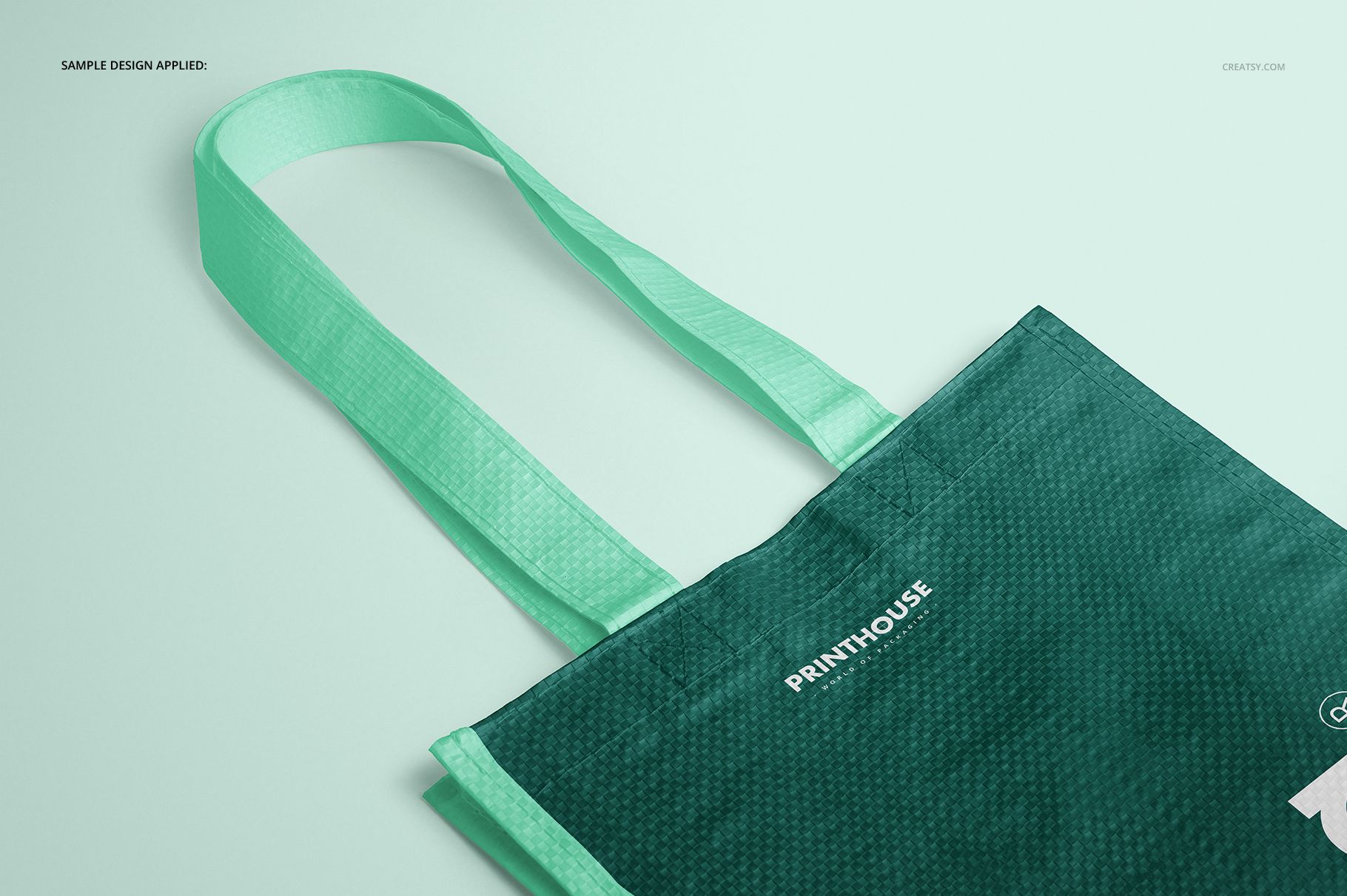 Front angled view of a woven tote bag mockup with mint green handles and a dark green textured body on a light background.