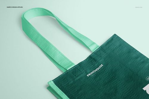 Front angled view of a woven tote bag mockup with mint green handles and a dark green textured body on a light background.