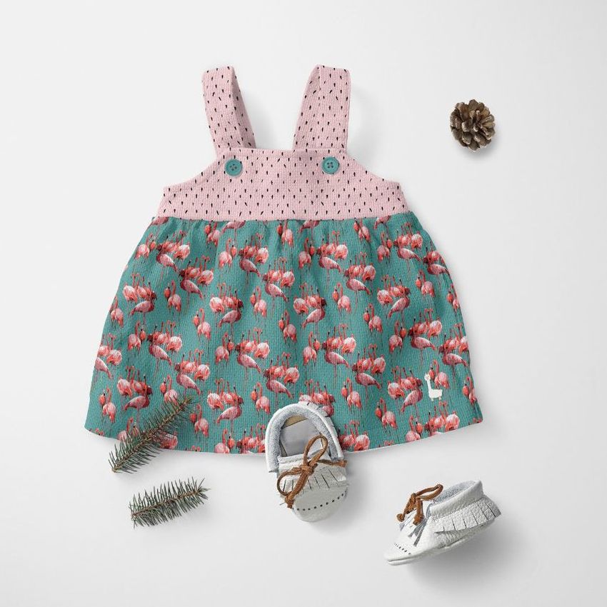 Baby dress mockup displayed flat on a white surface, featuring a pink and teal floral pattern with shoes and pinecone props.