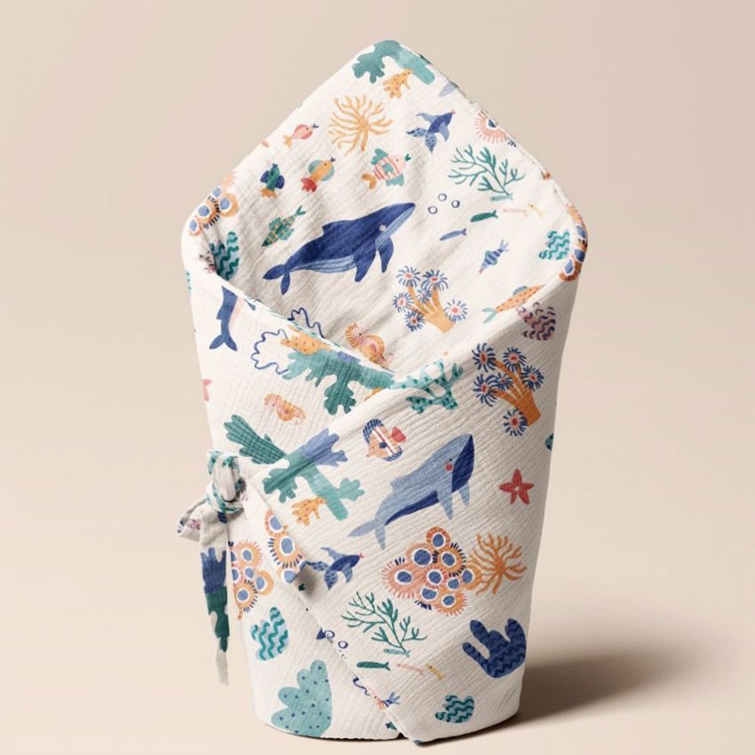 Newborn swaddle wrap mockup featuring an ocean-themed pattern with whales, coral, and sea plants on a neutral background.
