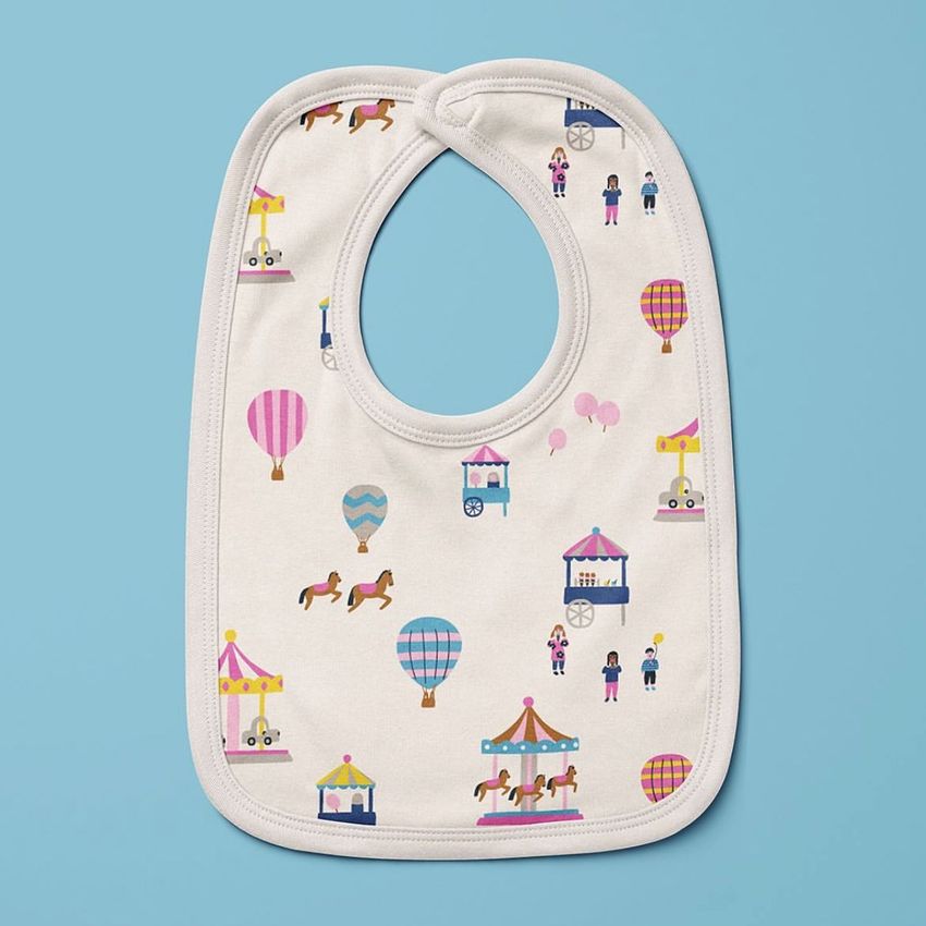 Velcro fastening bib mockup featuring a playful carousel and hot air balloon pattern on a light fabric, shown on a blue background.