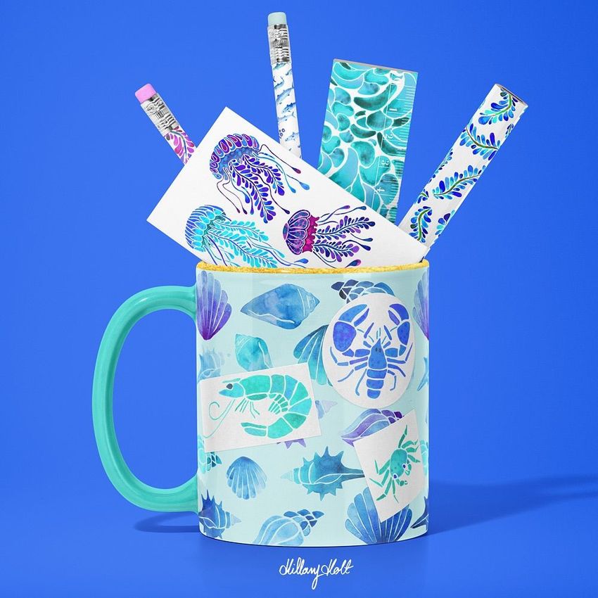 Mug mockup with a blue and turquoise sea life pattern, filled with pencils and stationery decorated with matching aquatic designs.