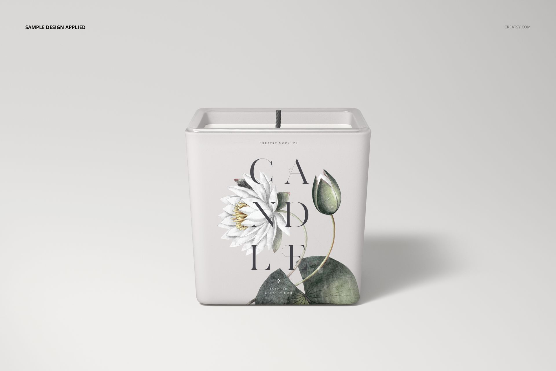 Front view of a square candle mockup with a botanical print and black wick, placed on a plain light backdrop.