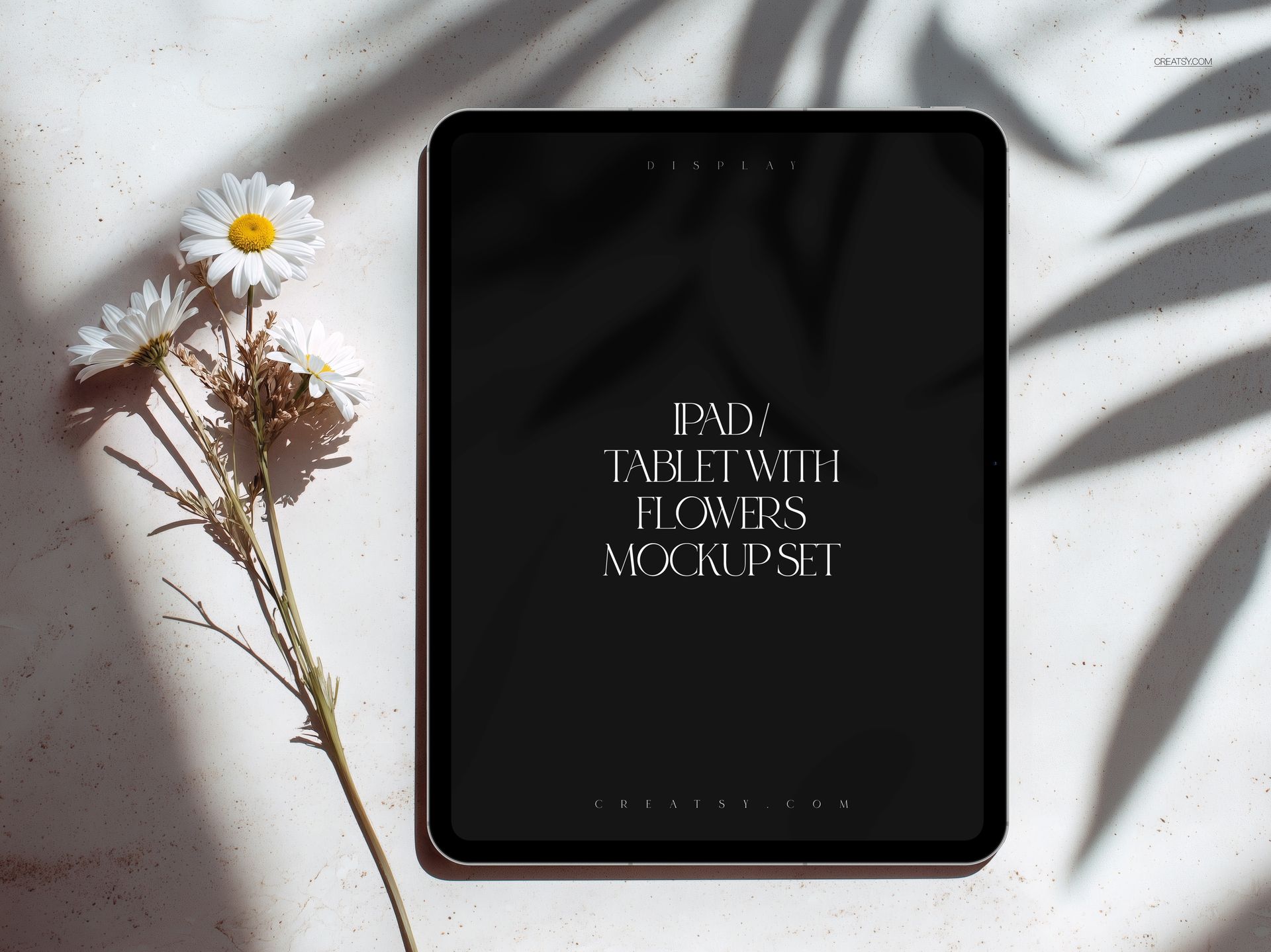 Front view of an iPad Pro mockup on a light surface with white daisies and leaf shadows beside the device.