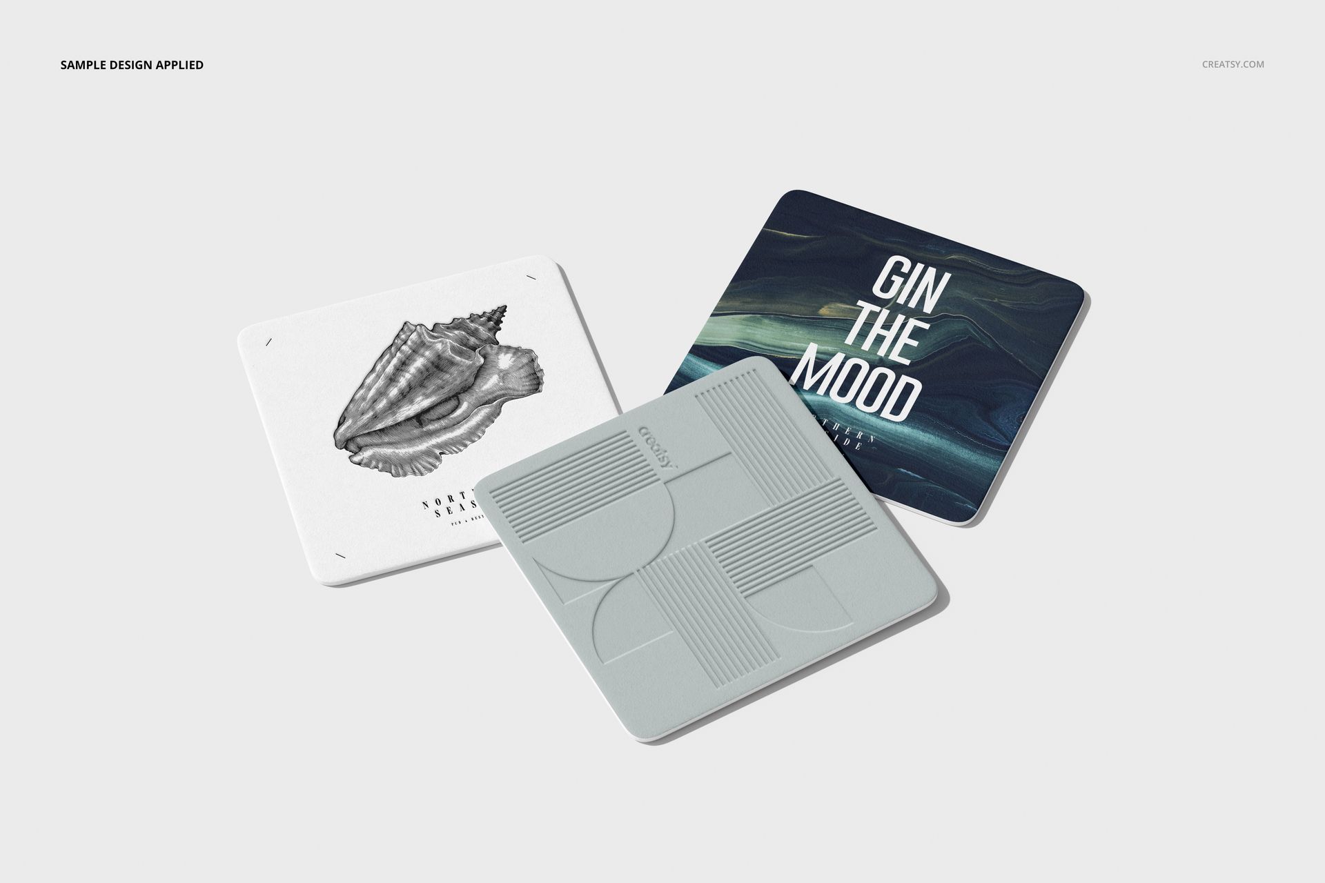 Square coasters mockup showing three coasters with unique artwork, viewed from above on a neutral background.