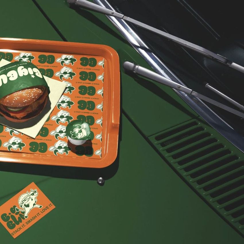 Burger branding mockup displayed on a green car hood, featuring a tray with a burger and colorful branded paper designs.