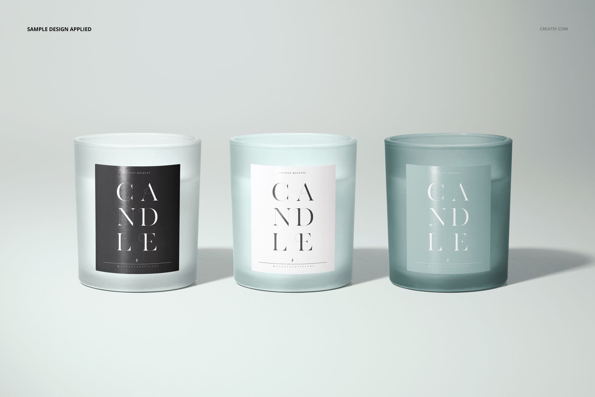Three frosted glass candle mockups with square paper labels, shown in a row against a neutral background.
