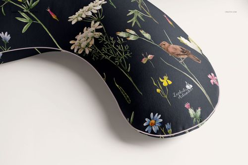 PSD mockup of a crescent-shaped pregnancy pillow with floral and bird patterns on a black surface, angled detail view.
