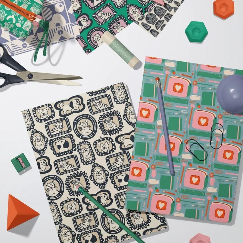 Stationery mockup showing two classic A4 notebooks with illustrated animal and geometric patterns, surrounded by office supplies.
