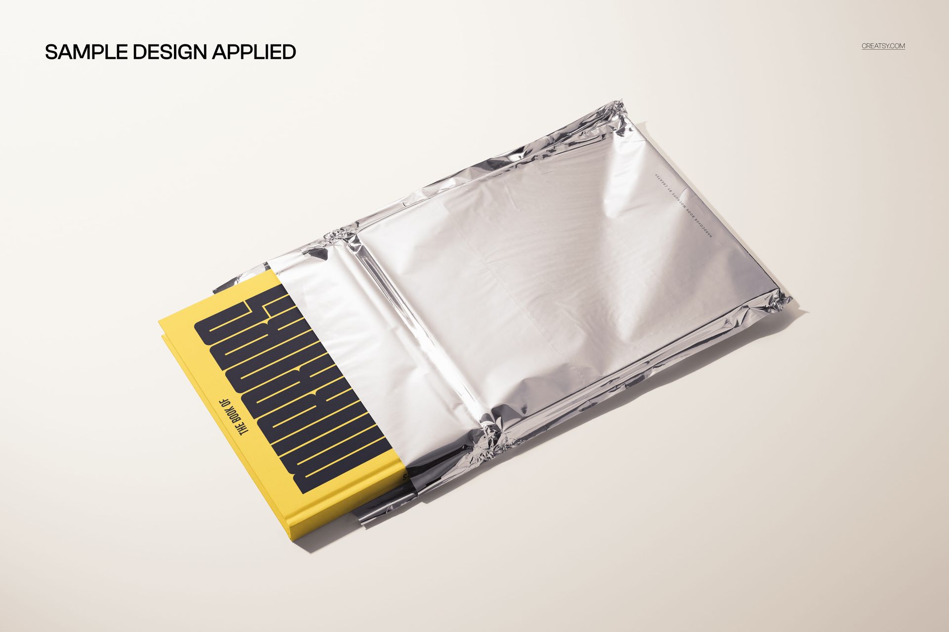 PSD mockup showing a hardback book with a graphic cover peeking out of a reflective metallic foil mailer.