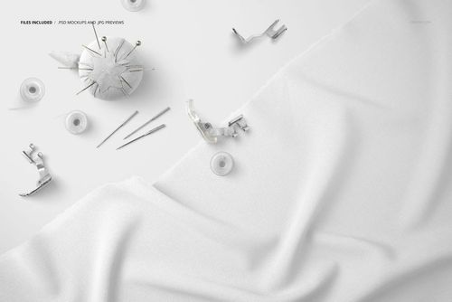 Top view of white textile fabric mockup with scattered sewing tools such as pins, bobbins, and metal presser feet.