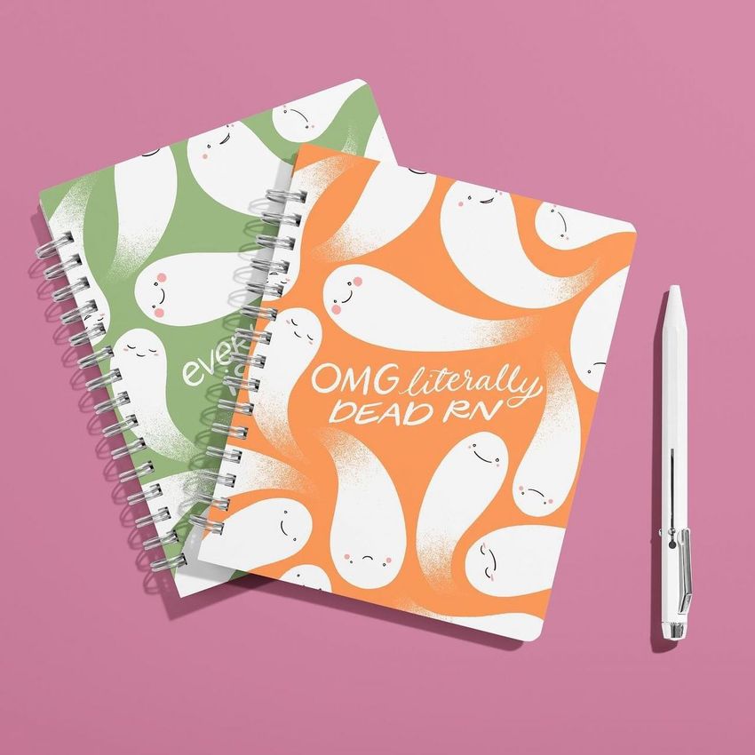 Spiral-bound notebook mockup set featuring orange and green covers with cute ghost illustrations on a solid pink background.