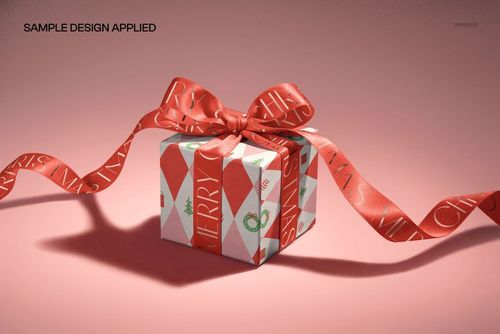 Front view of a cube-shaped gift box mockup featuring a festive red ribbon and geometric holiday print on a pink background.